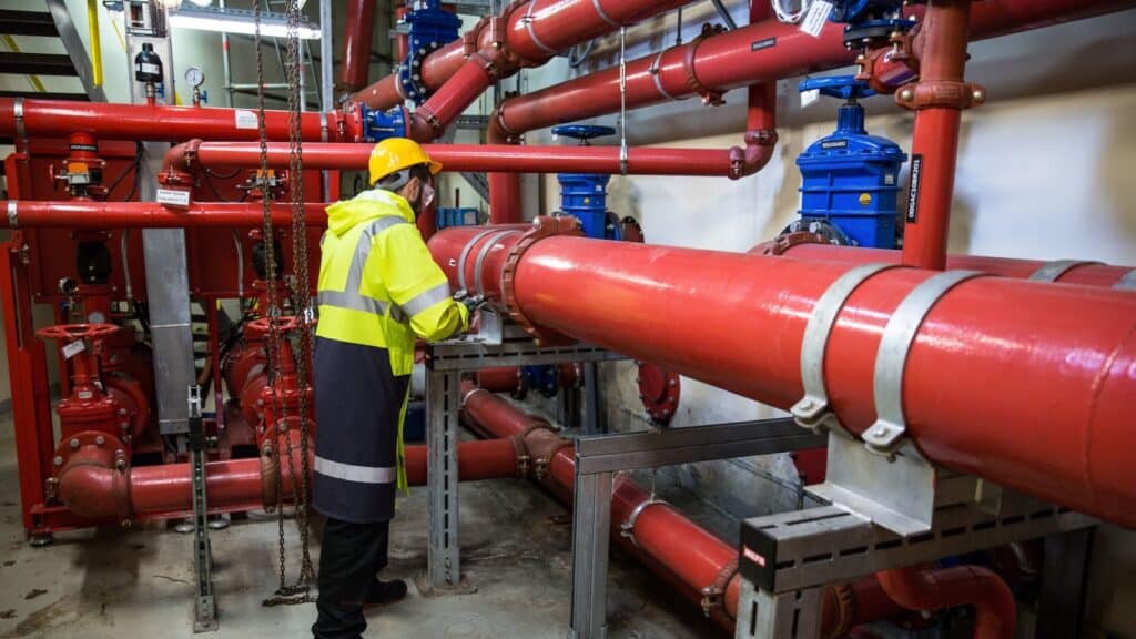 Engineer wearing safety gear inspecting red industrial piping system indoors